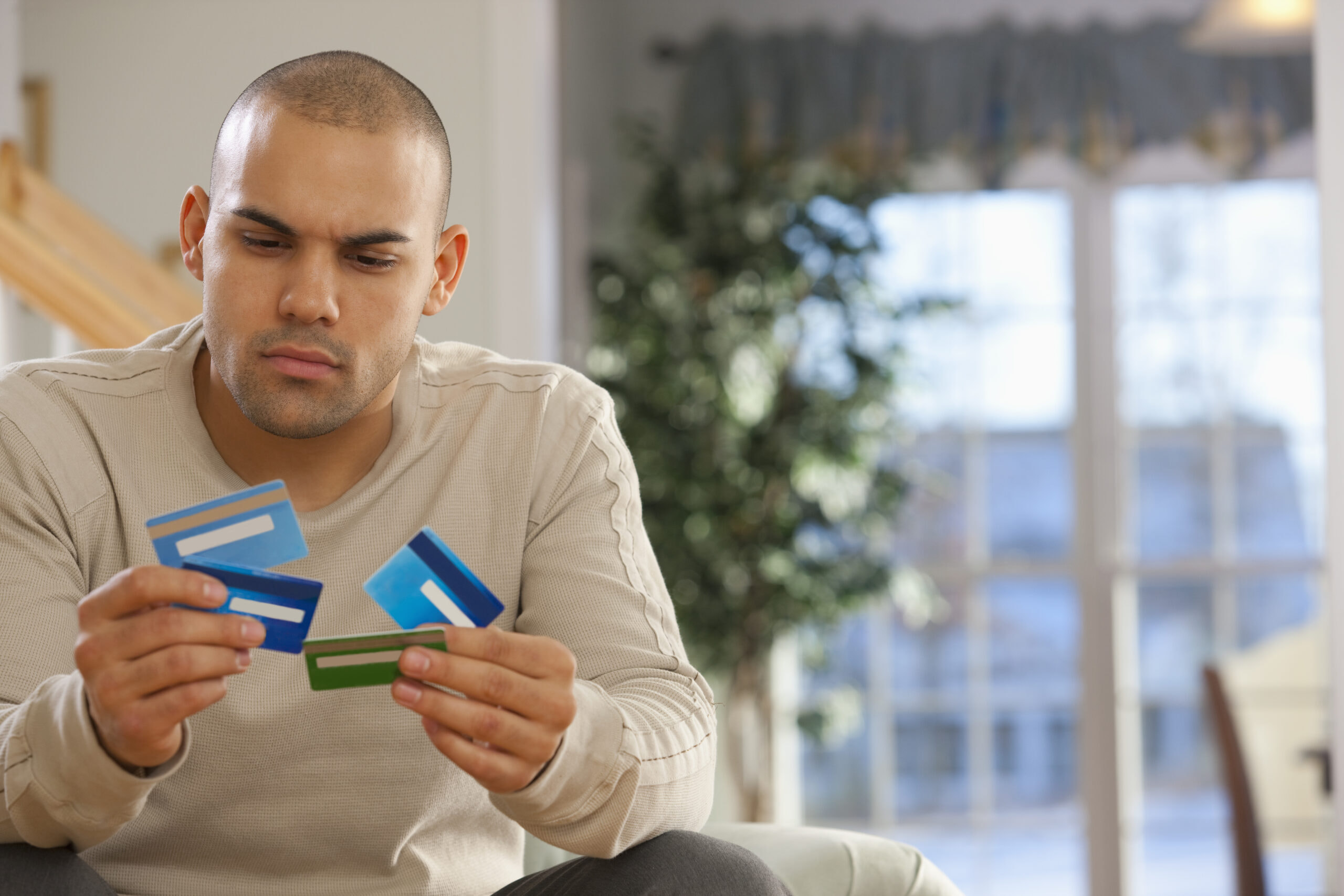 Man sitting indoors looking concerned while holding multiple credit cards in his hands